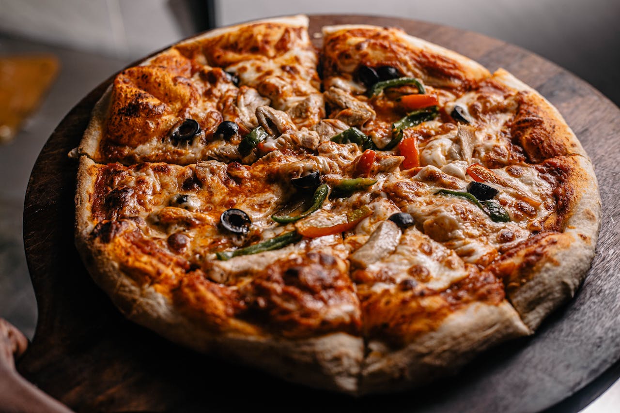 Close-up of a freshly-baked vegetable pizza with olives, peppers, and mushrooms on a wooden board.